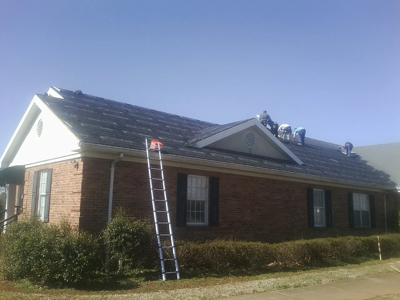 Crew tearing shingles off a brick ranch roof with a ladder set — Metal Roof Repair work by our crew in Covington