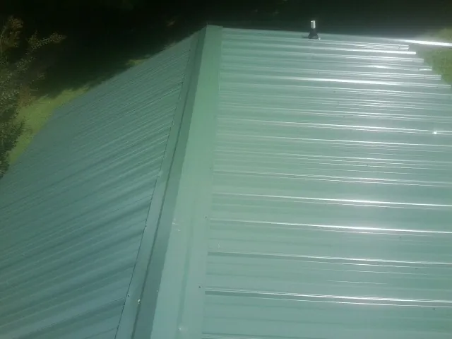 New green metal panels meeting at the ridge of a roof — Flat Roof Repair work by our crew in Covington